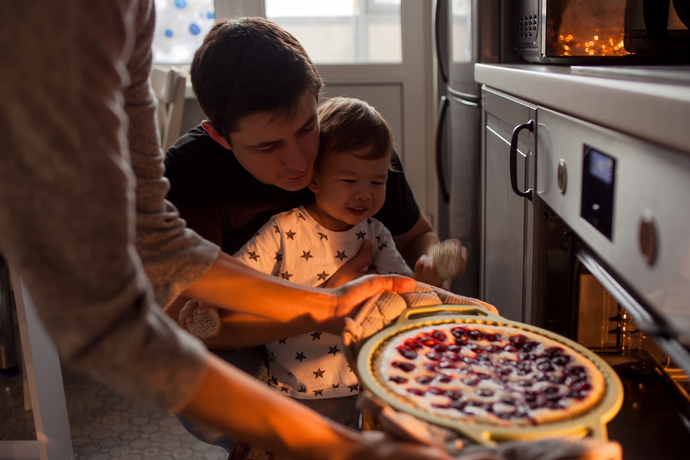 young family making a cake together. Mom dad and son pull the cake out of the oven