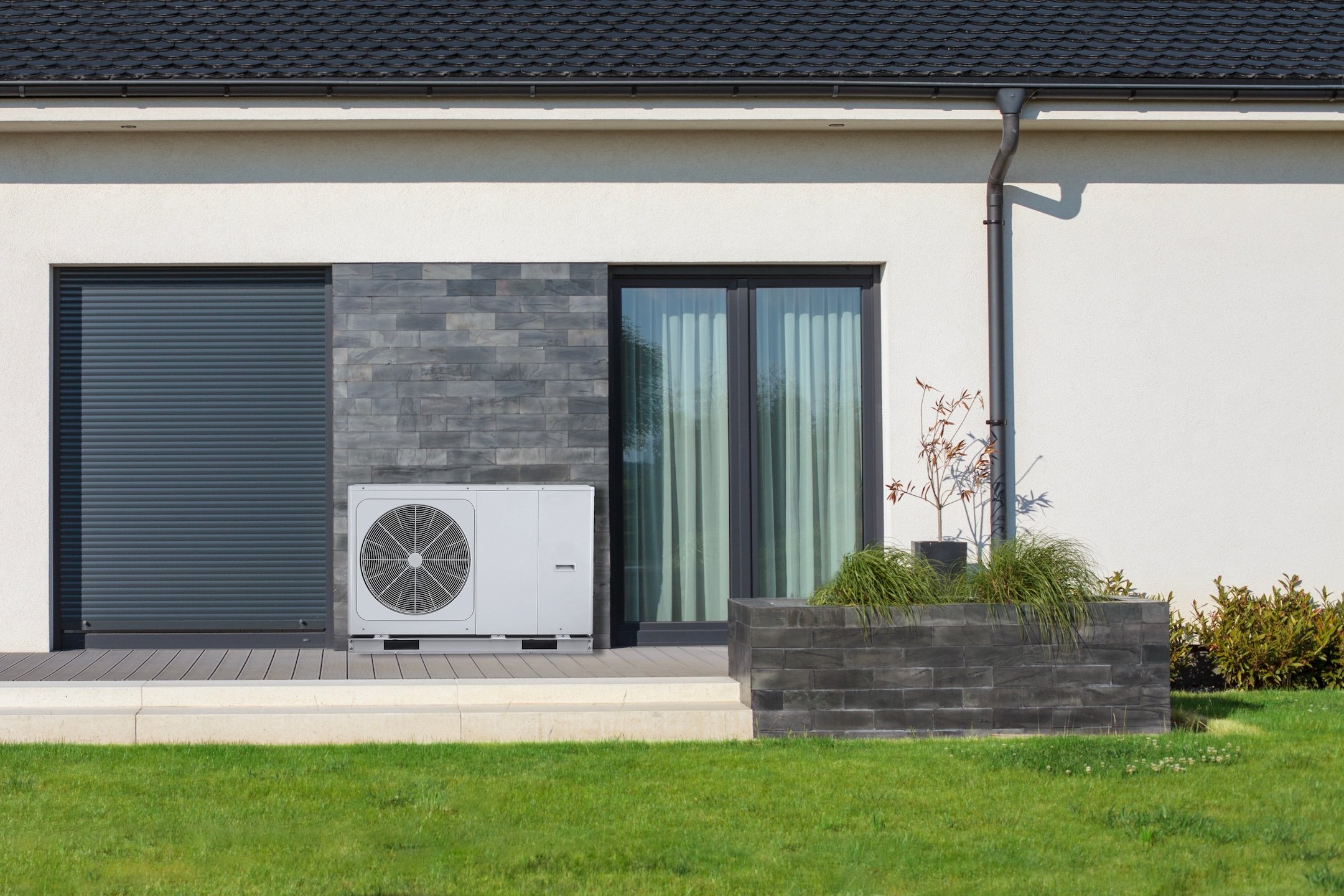 An ecological air heat pump stands beside a modern house with a lush lawn, showcasing sustainable and eco-friendly heating solutions.
